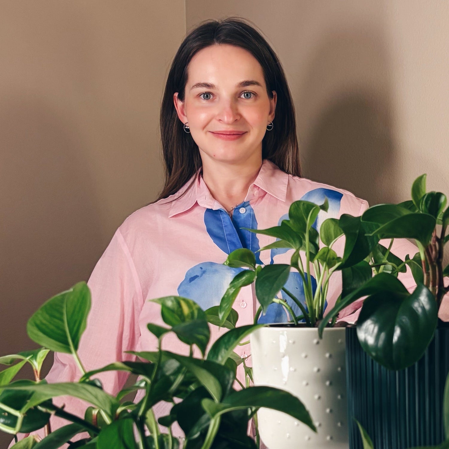 Woman standing behind a variety of potted plants indoors.